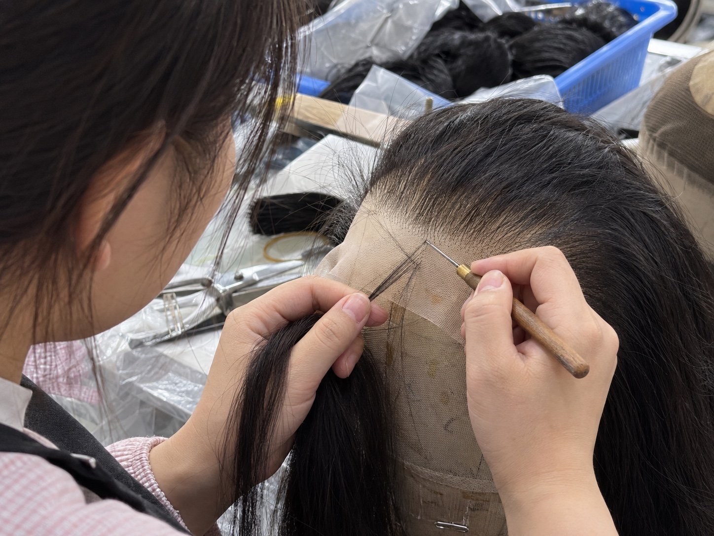 Close-up illustration of a worker using a ventilating needle to tie hair into a lace wig front