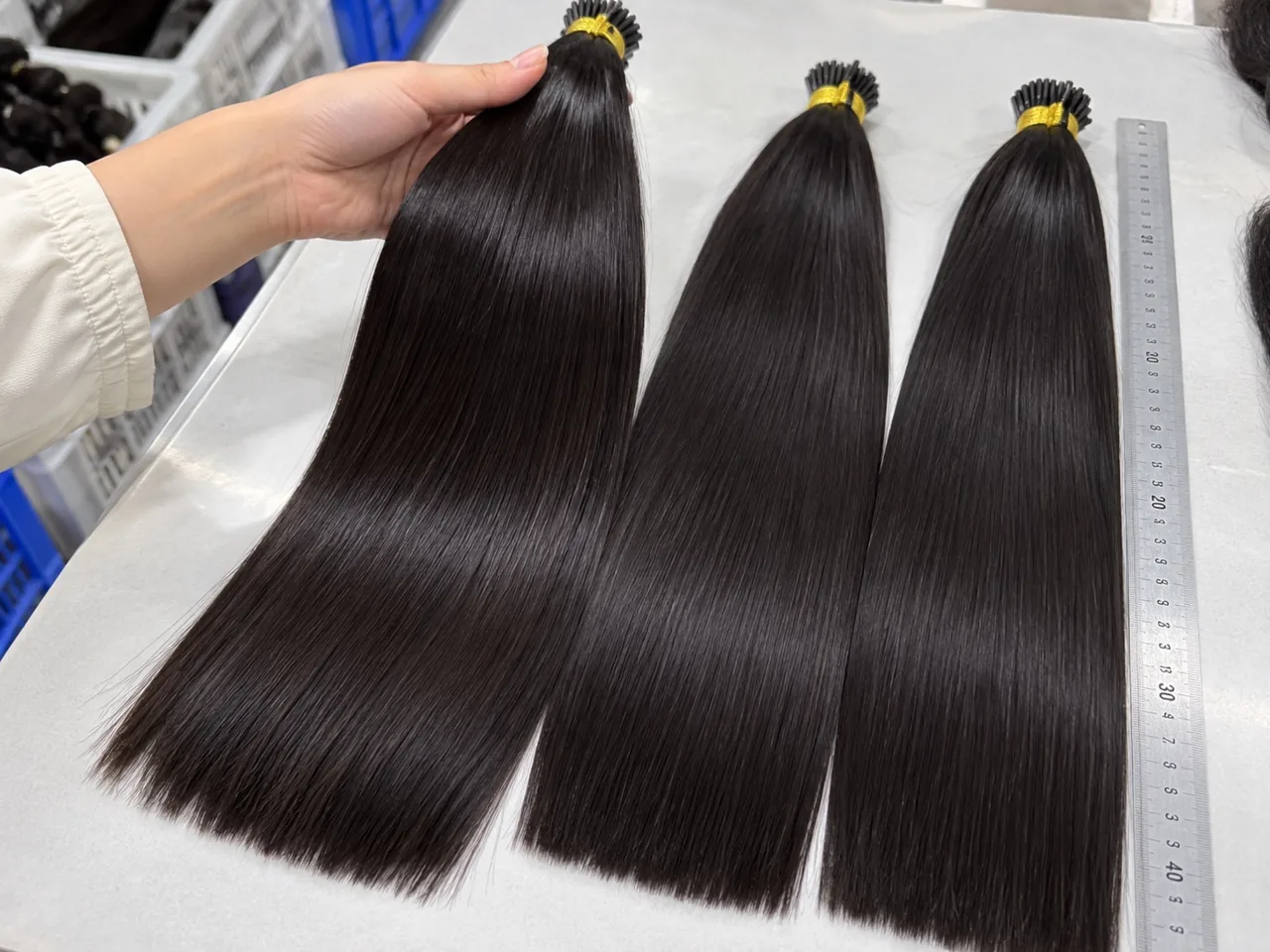 Three straight hair samples beside a ruler with one sample held by hand
