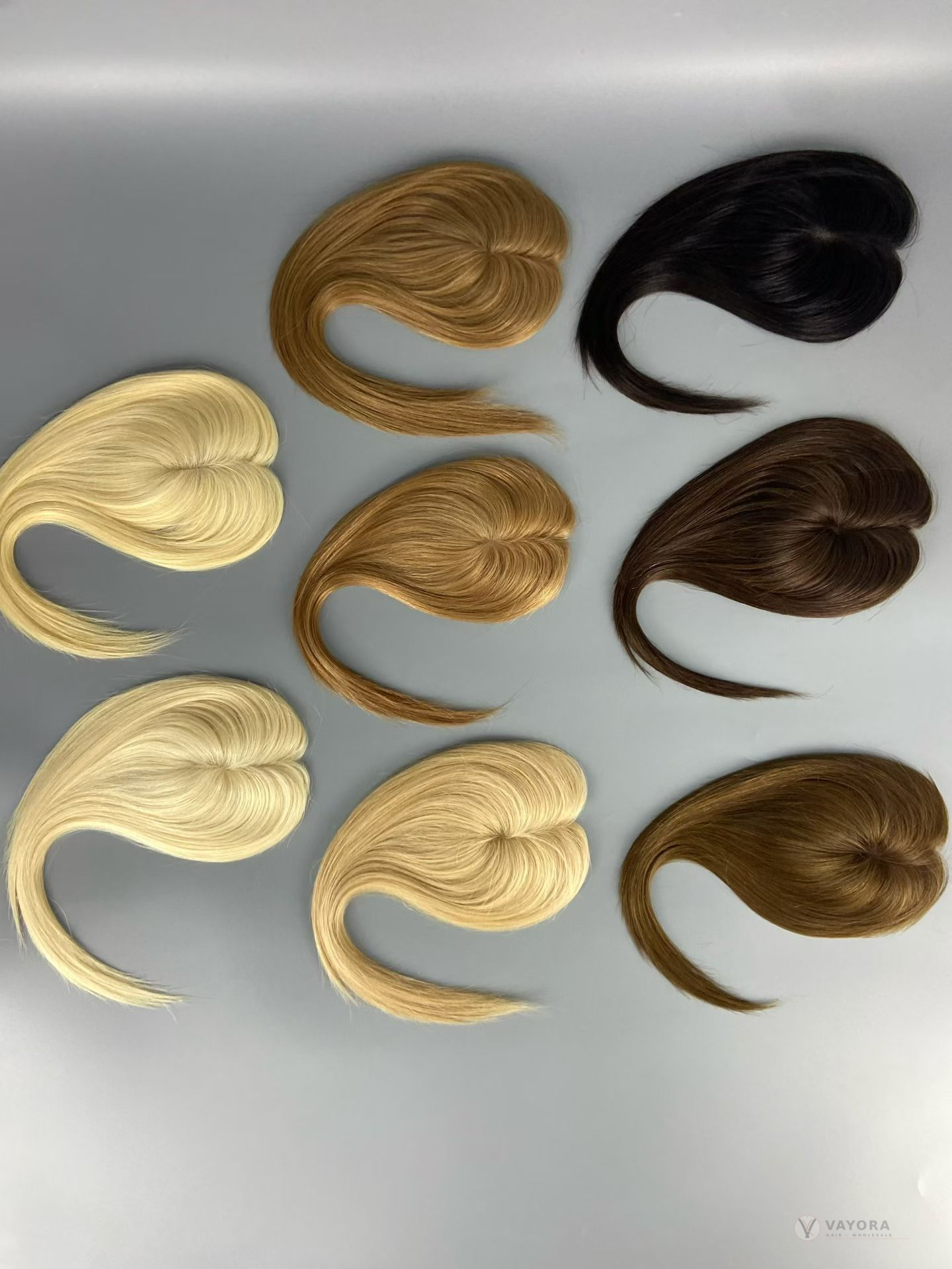 Eight loose hair bundles in blonde, brown and dark shades arranged on a grey surface