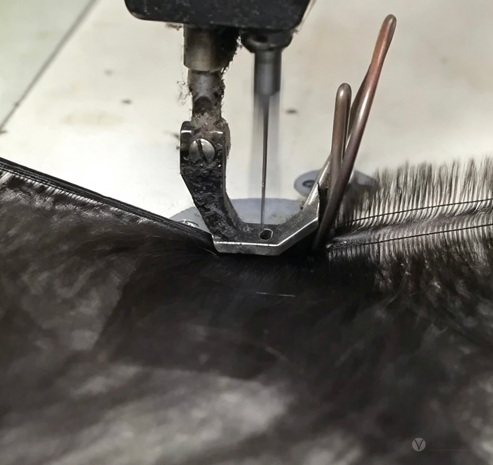 Close-up of a sewing machine needle and stitching along the edge of dark hair.